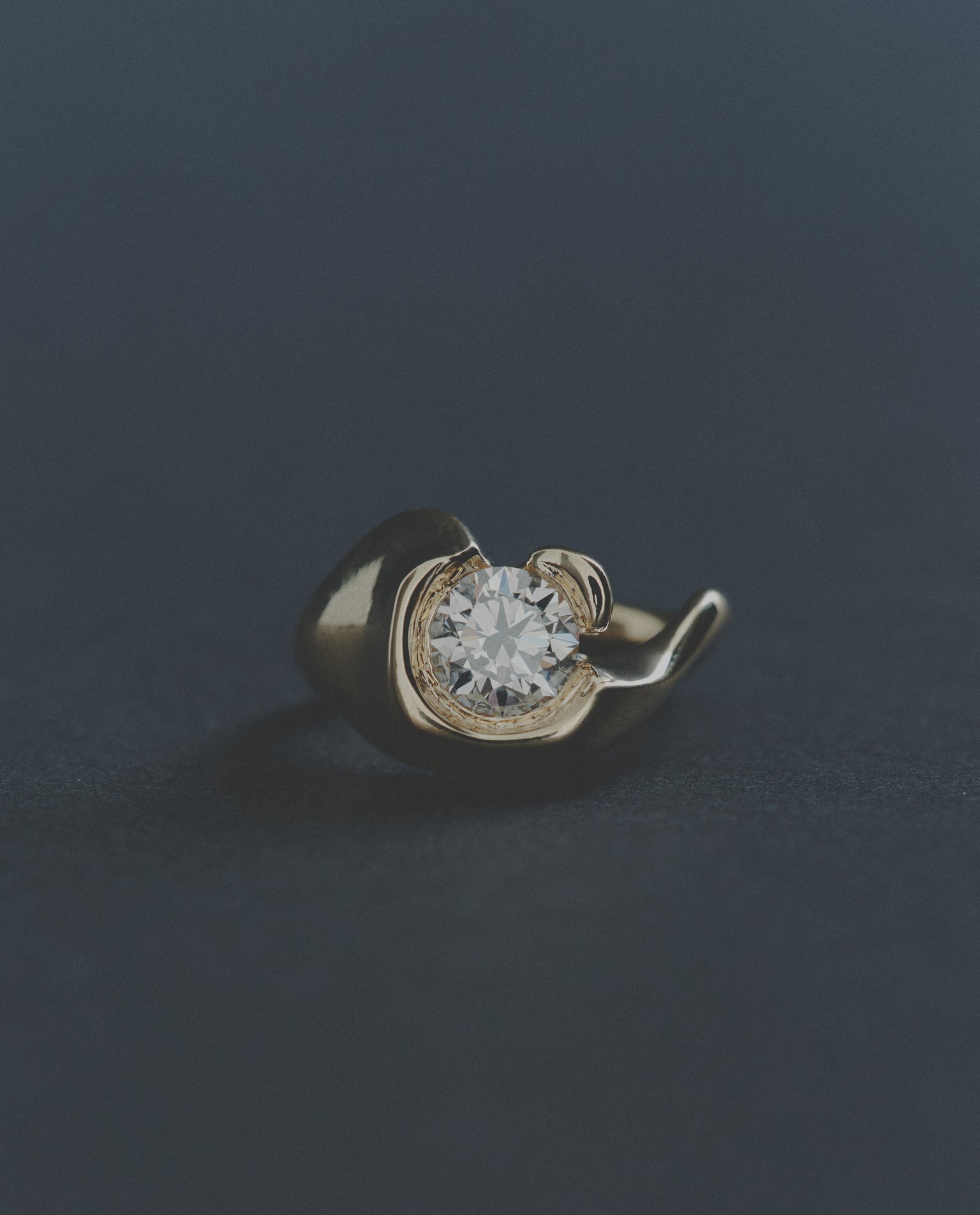 Gold ring with a round diamond on a dark background