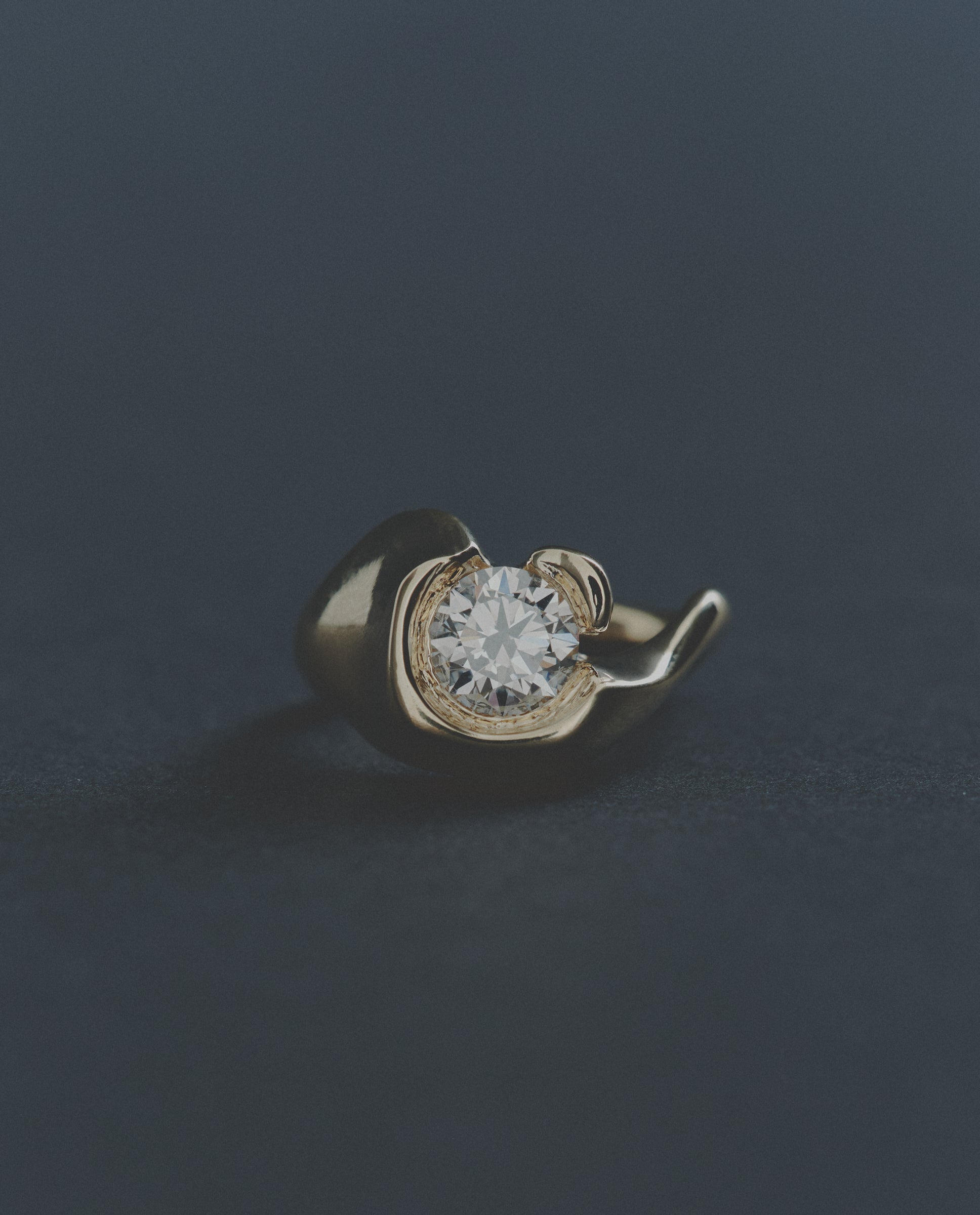 Gold ring with a round diamond on a dark background