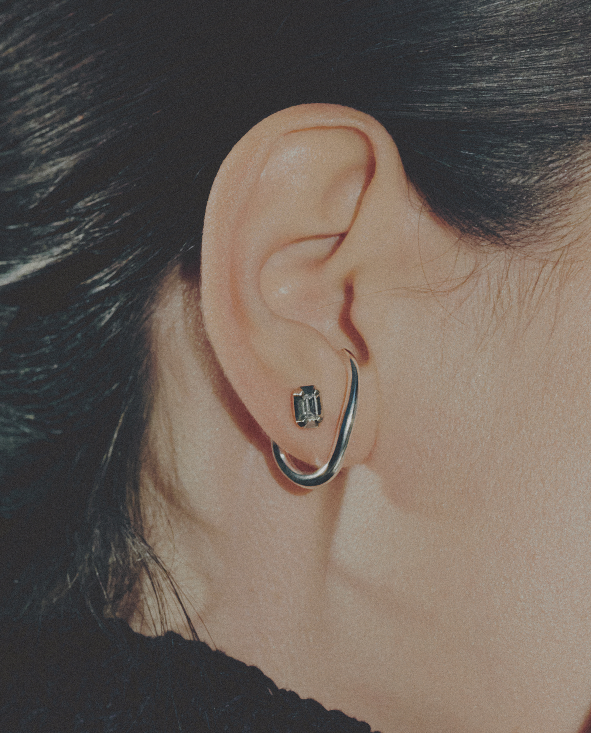 Close-up of an ear wearing a silver hoop earring with a small gemstone.