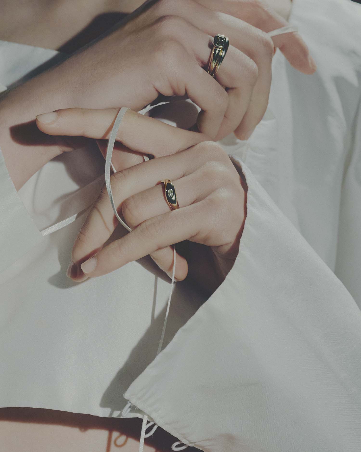 Close-up of hands with gold rings on a light background.
