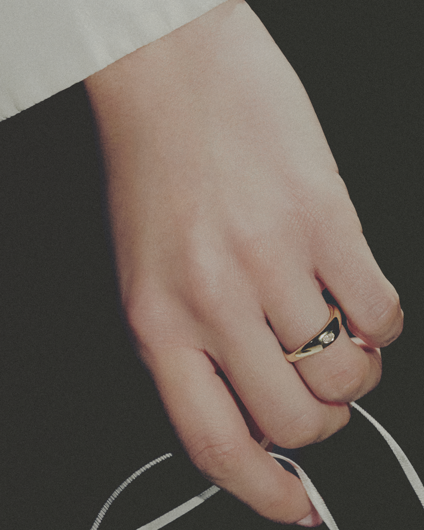 Hand wearing a gold ring on a dark background