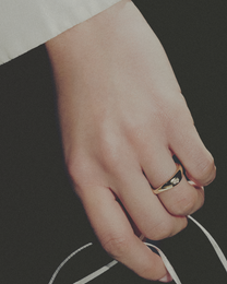 Hand wearing a gold ring on a dark background