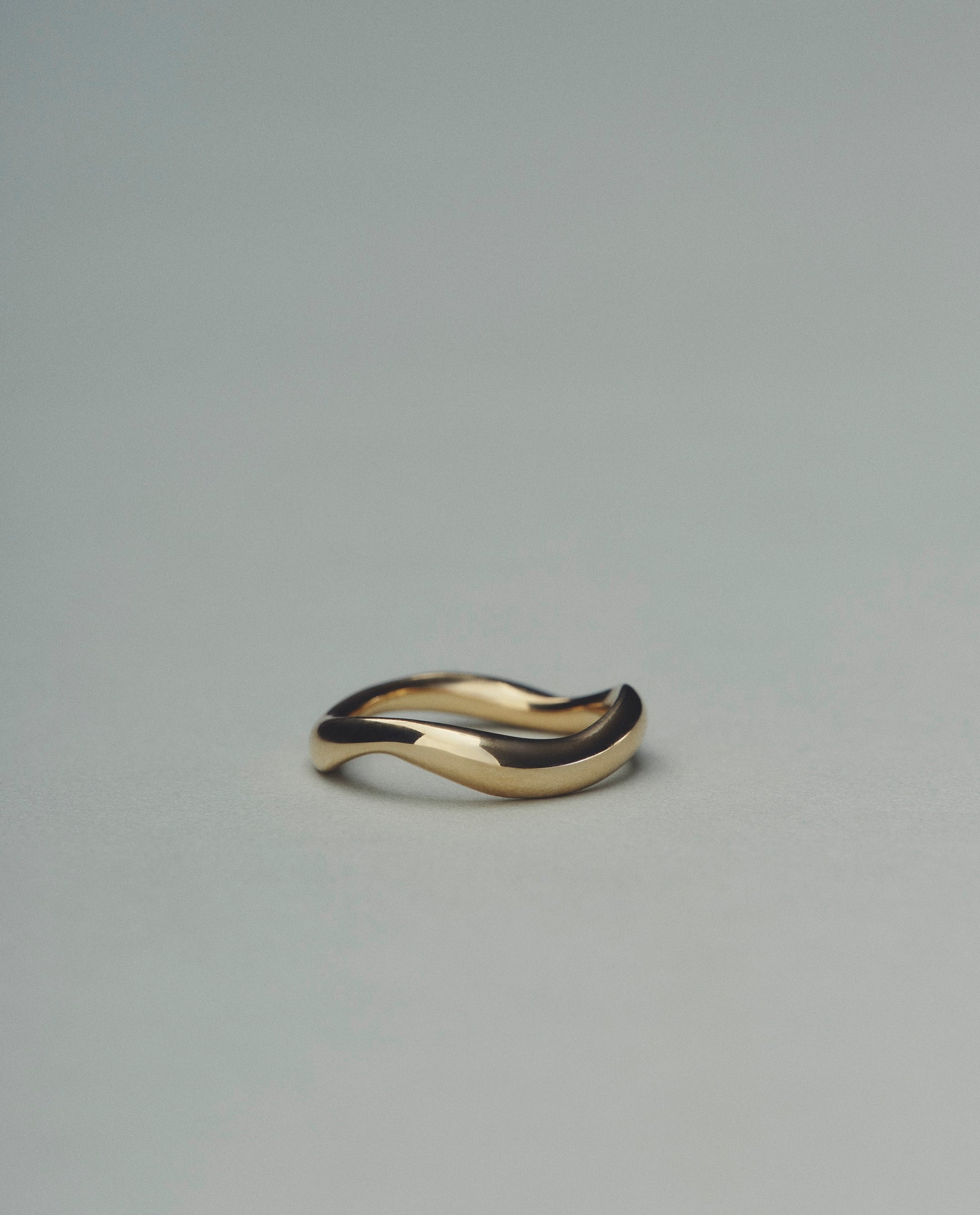 Gold ring with a wavy design on a gray background