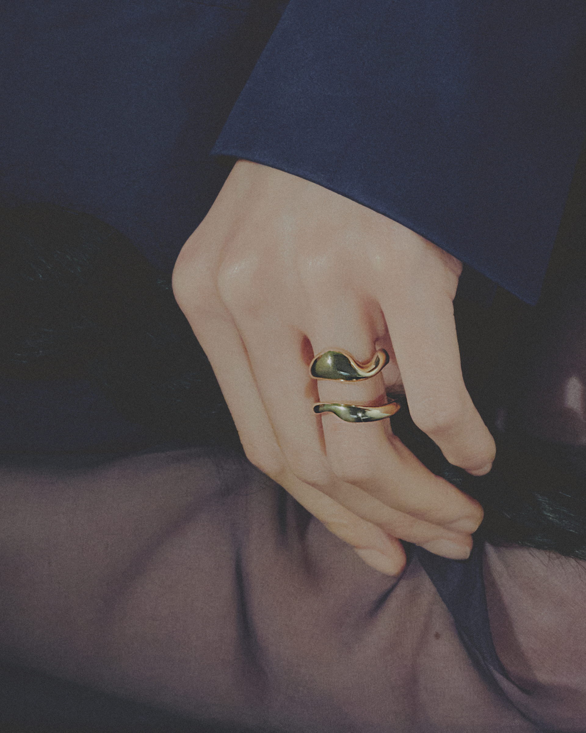 Close-up of a hand wearing two gold rings with a dark background