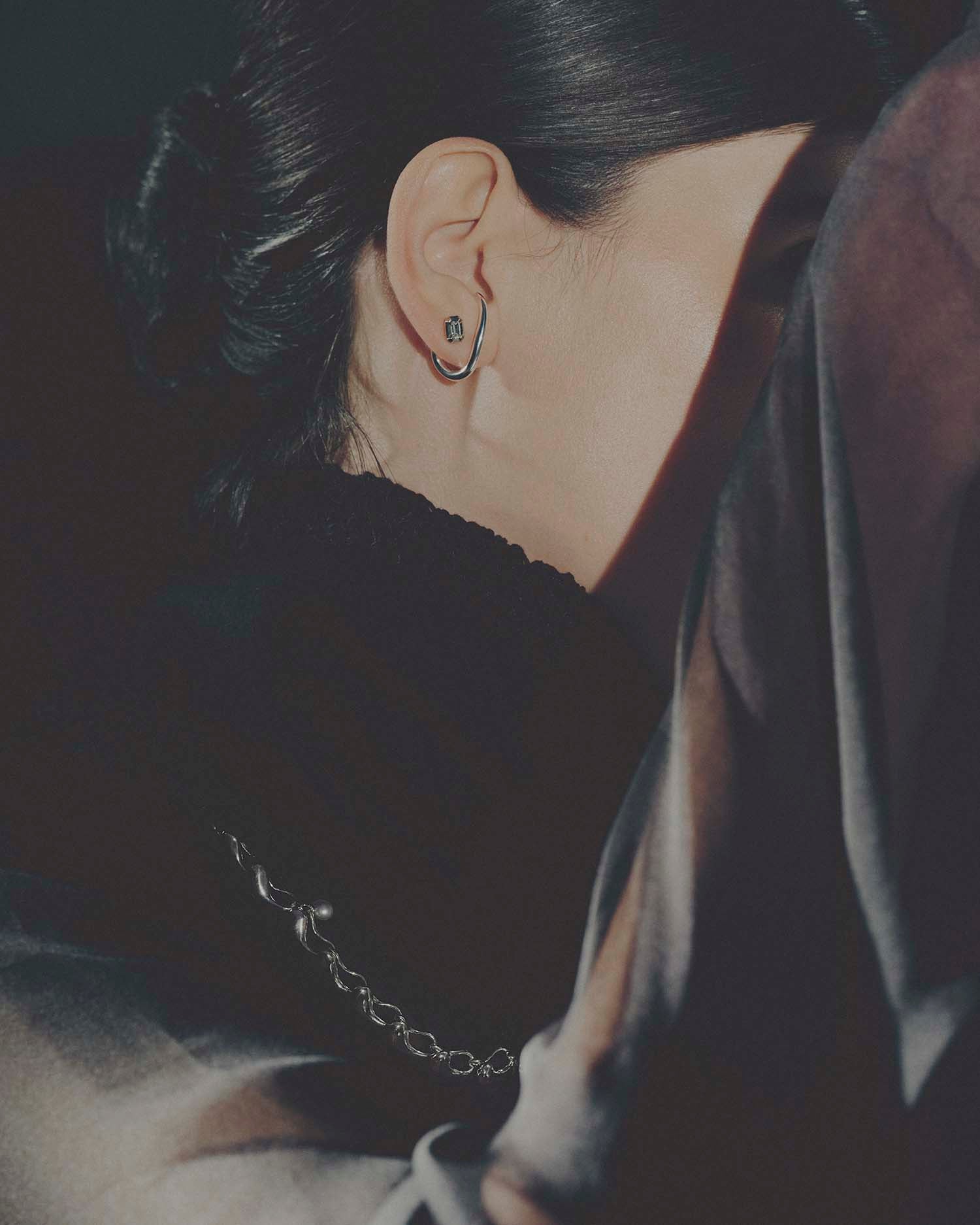 Close-up of an ear with a diamond stud and cuff earring on a dark background