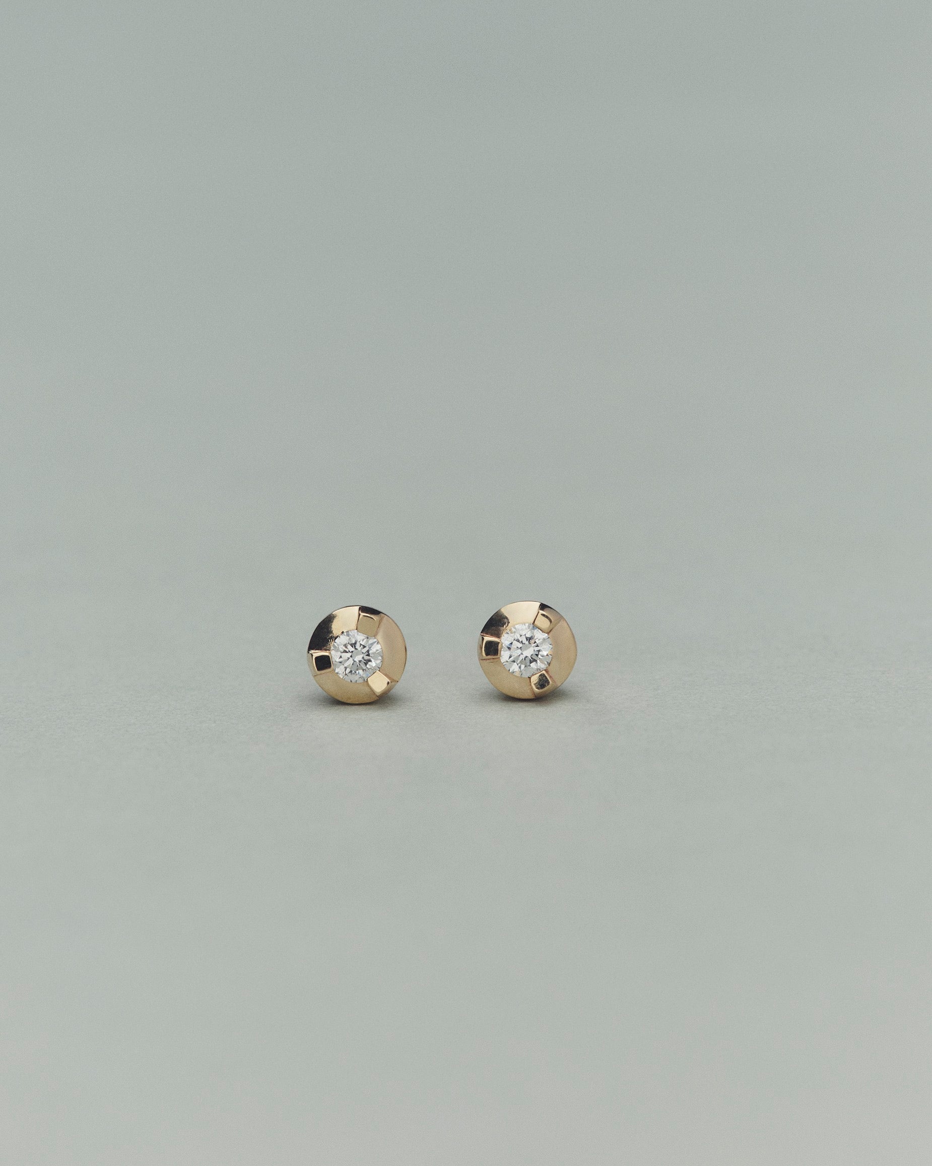Pair of gold earrings with embedded diamonds on a light gray background