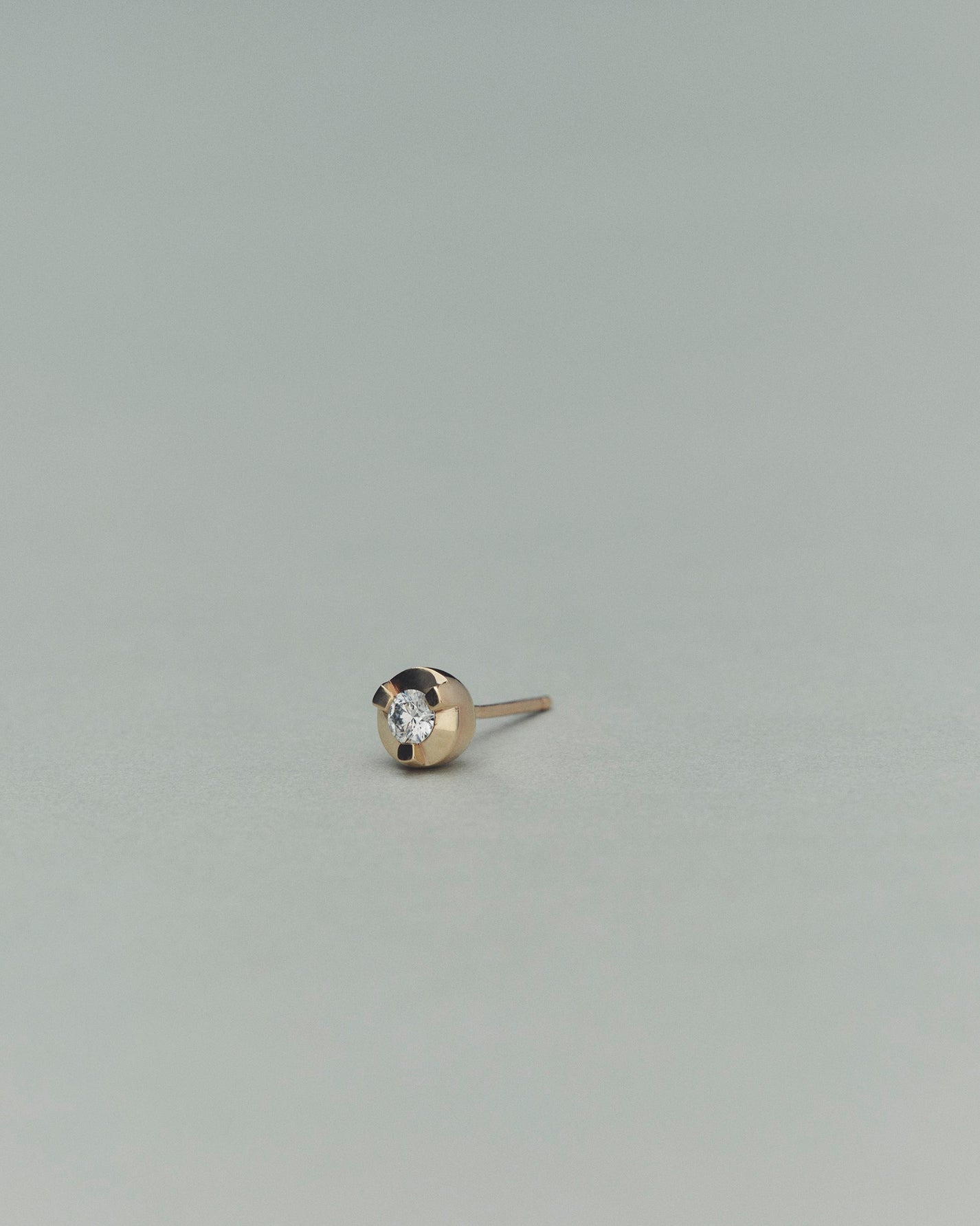Gold earring with a diamond on a light gray background