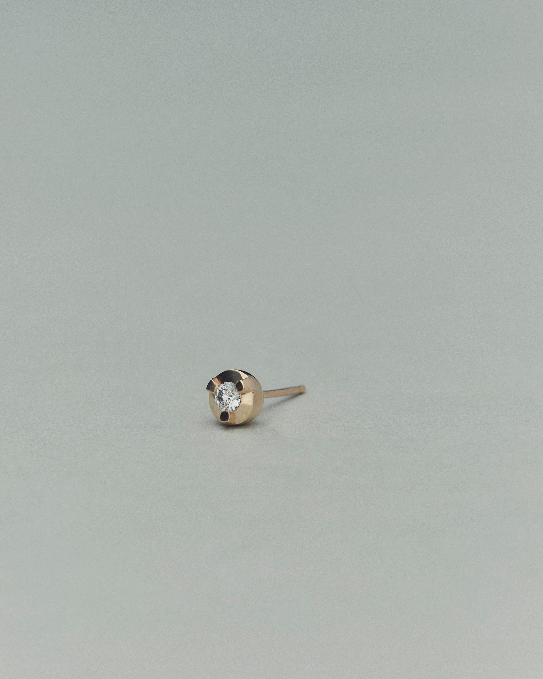 Gold earring with a diamond on a light gray background