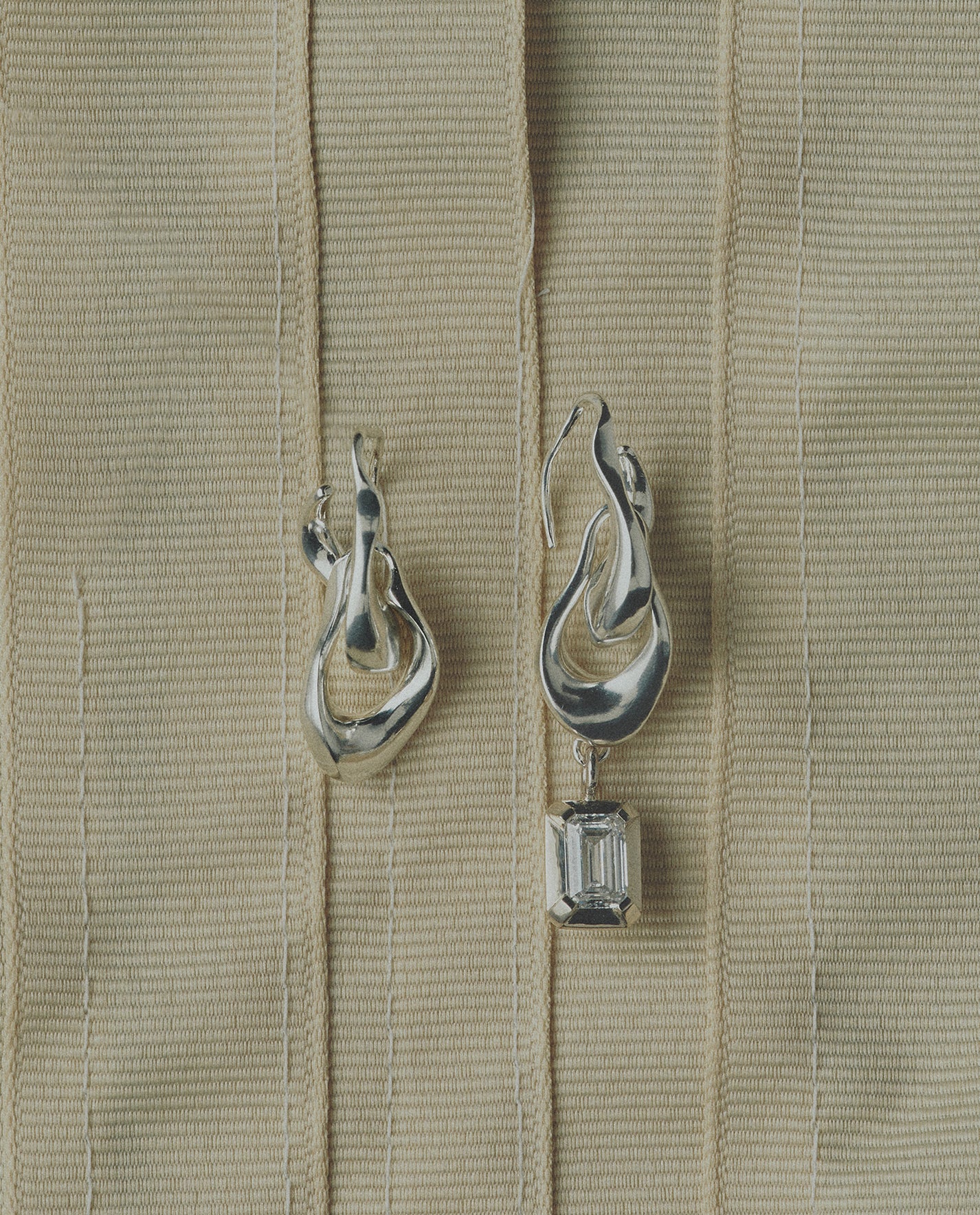 Pair of silver earrings one featuring a diamond on a beige ribbon background