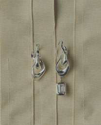 Pair of silver earrings one featuring a diamond on a beige ribbon background