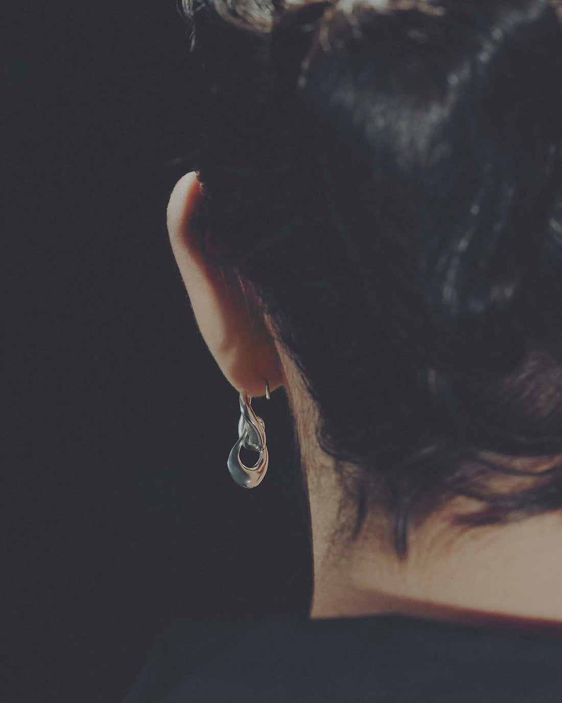 Close-up of an ear from behind with a silver earring against a dark background
