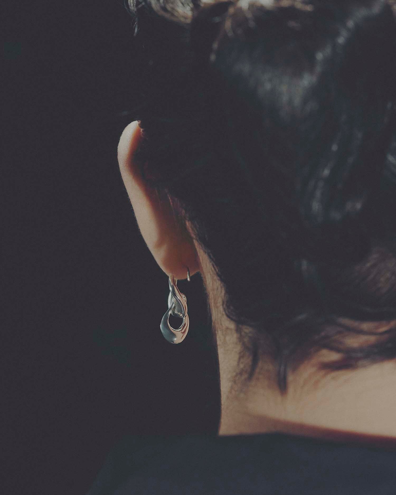 Close-up of an ear from behind with a silver earring against a dark background