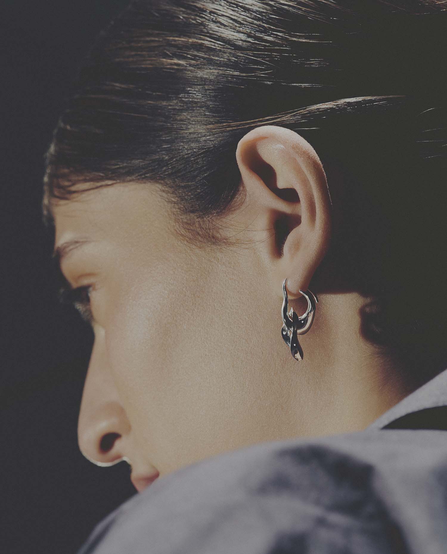Close-up of a person wearing a silver earring with a dark background