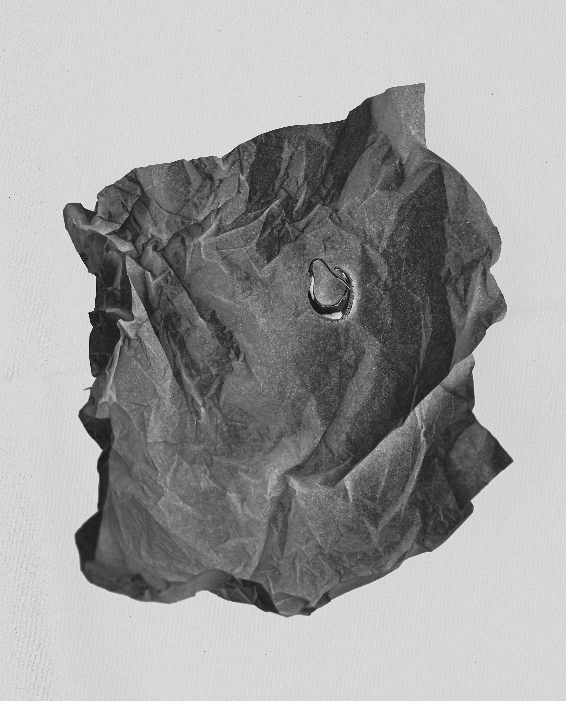 Black crumpled paper ball with hoop earring resting on a light gray background