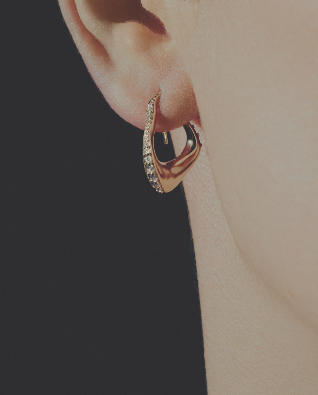 Gold diamond hoop earring worn on an ear with a plain background