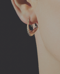Gold diamond hoop earring worn on an ear with a plain background