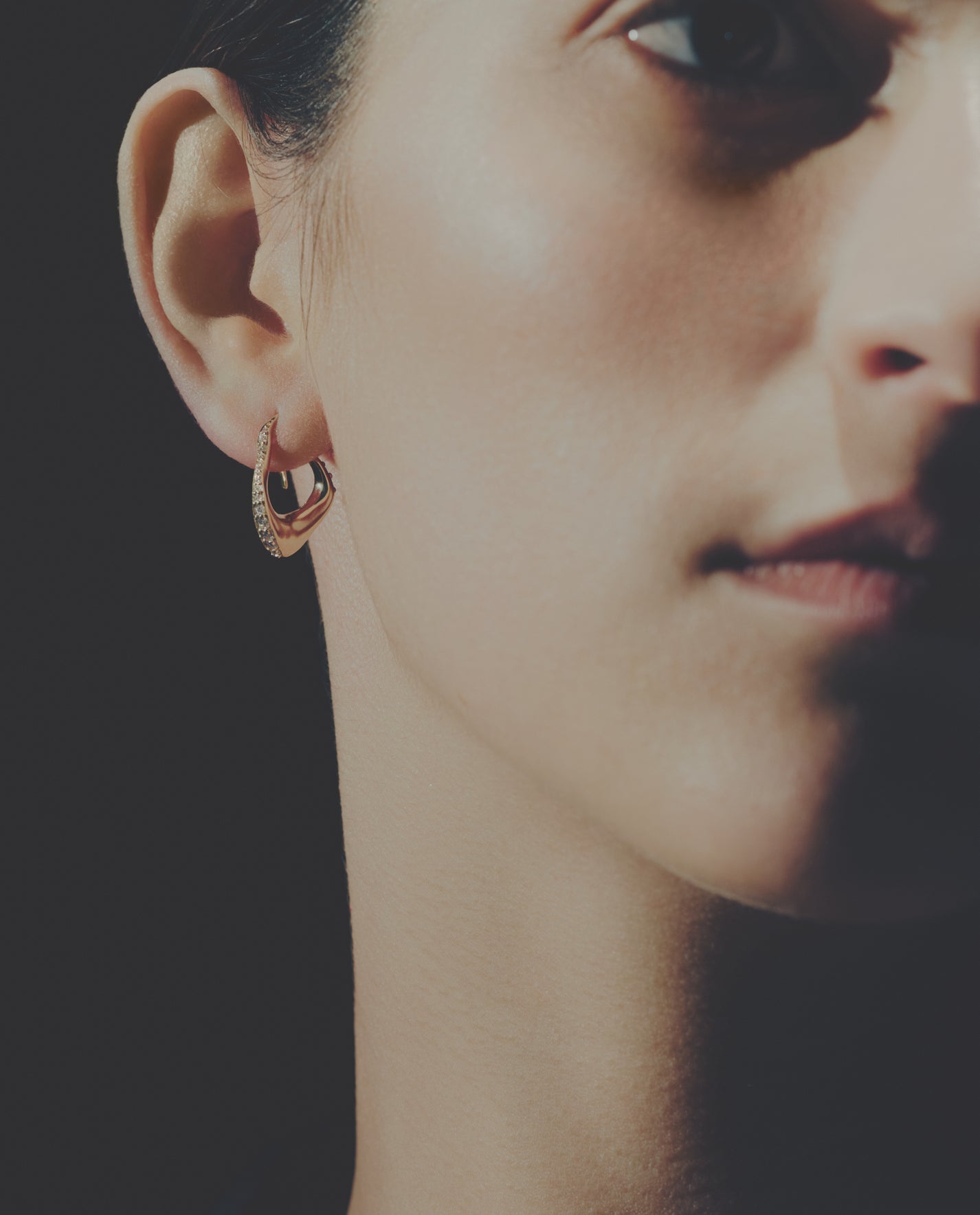 Close-up of a person wearing a gold diamond earring with a dark background