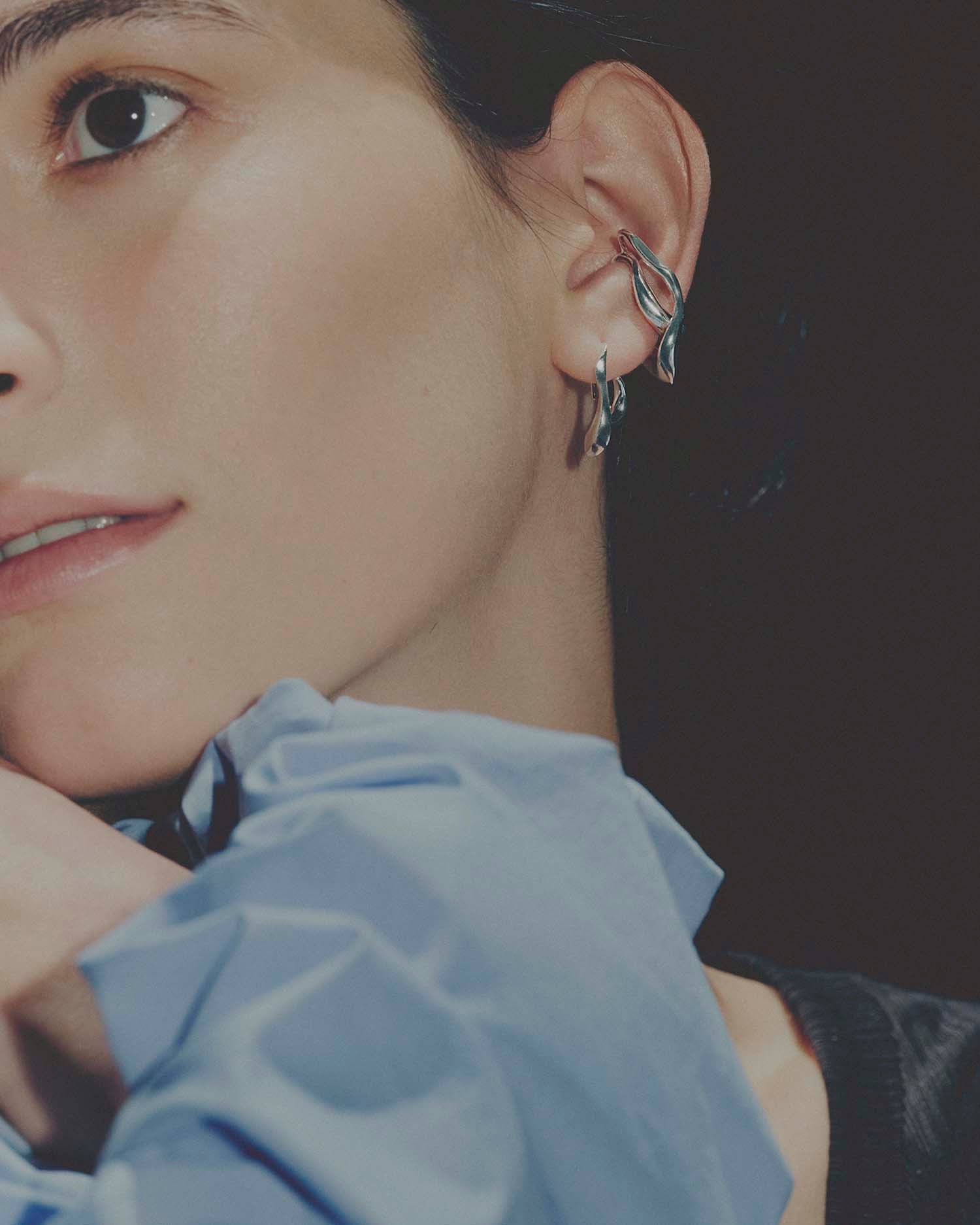 Close-up of a person wearing two silver earrings with a dark background