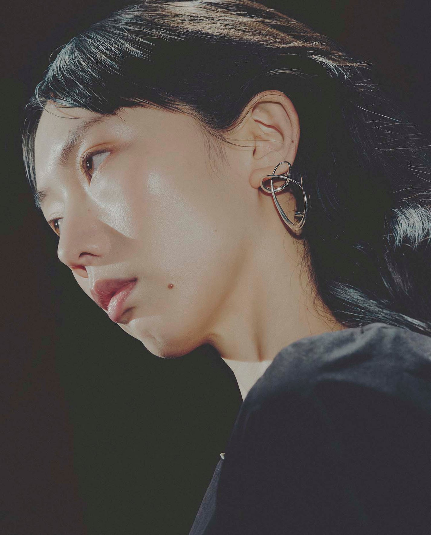 Close-up of a person wearing a unique earring against a dark background