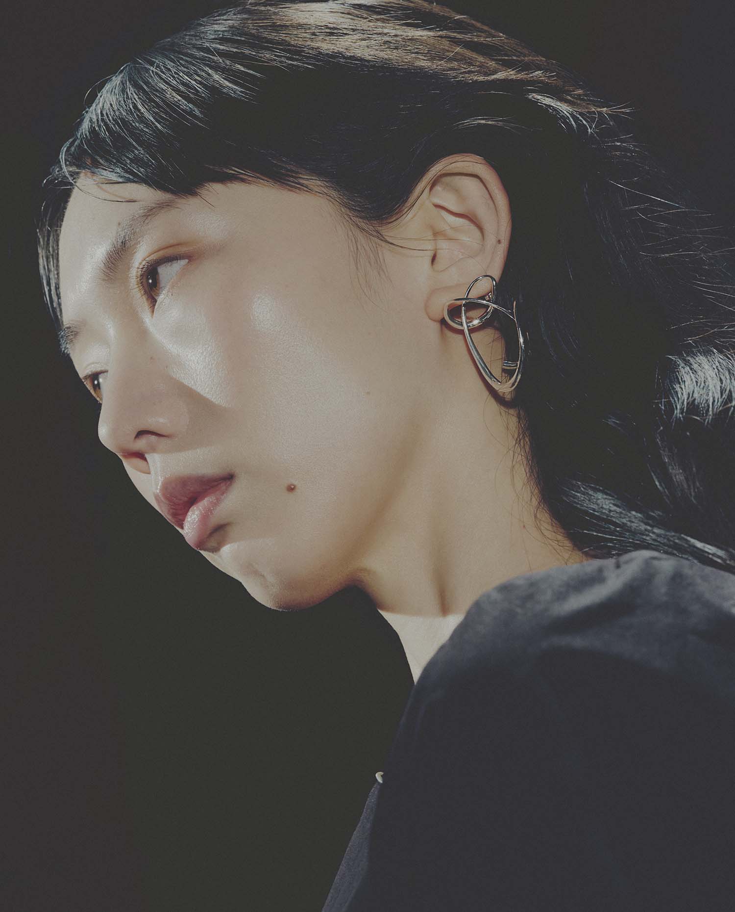 Close-up of a person wearing a unique earring against a dark background