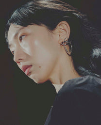 Close-up of a person wearing a unique earring against a dark background