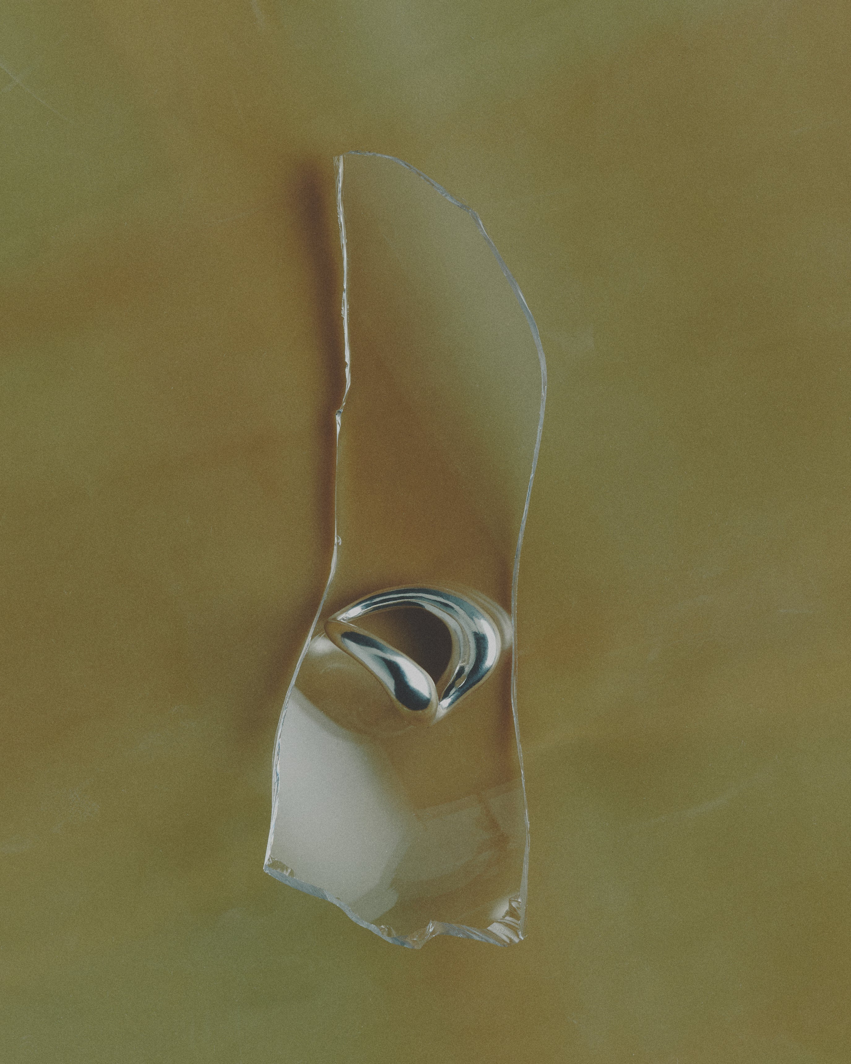 Broken glass piece with silver ring resting on top on a yellow background