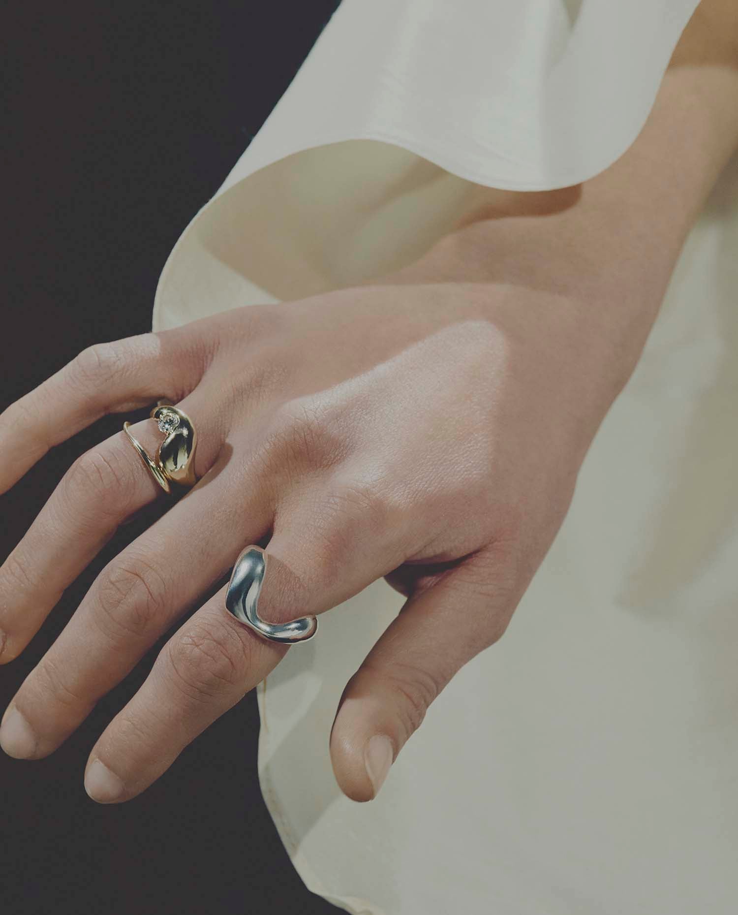 Close-up of a hand wearing three rings on a plain background