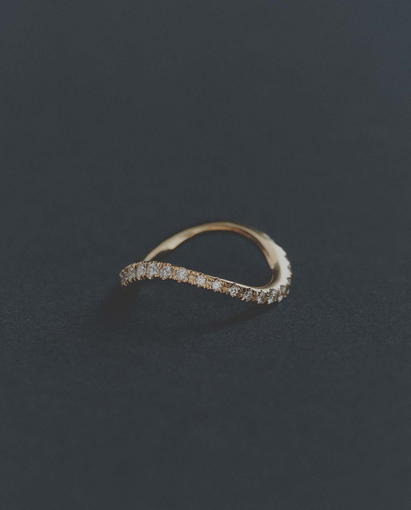 Delicate gold ring with small diamonds on a dark gray background