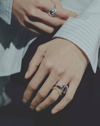 Close-up of hands wearing silver and gold rings on a dark background
