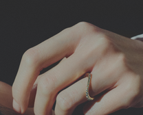Close-up of a hand wearing a gold ring on a dark background