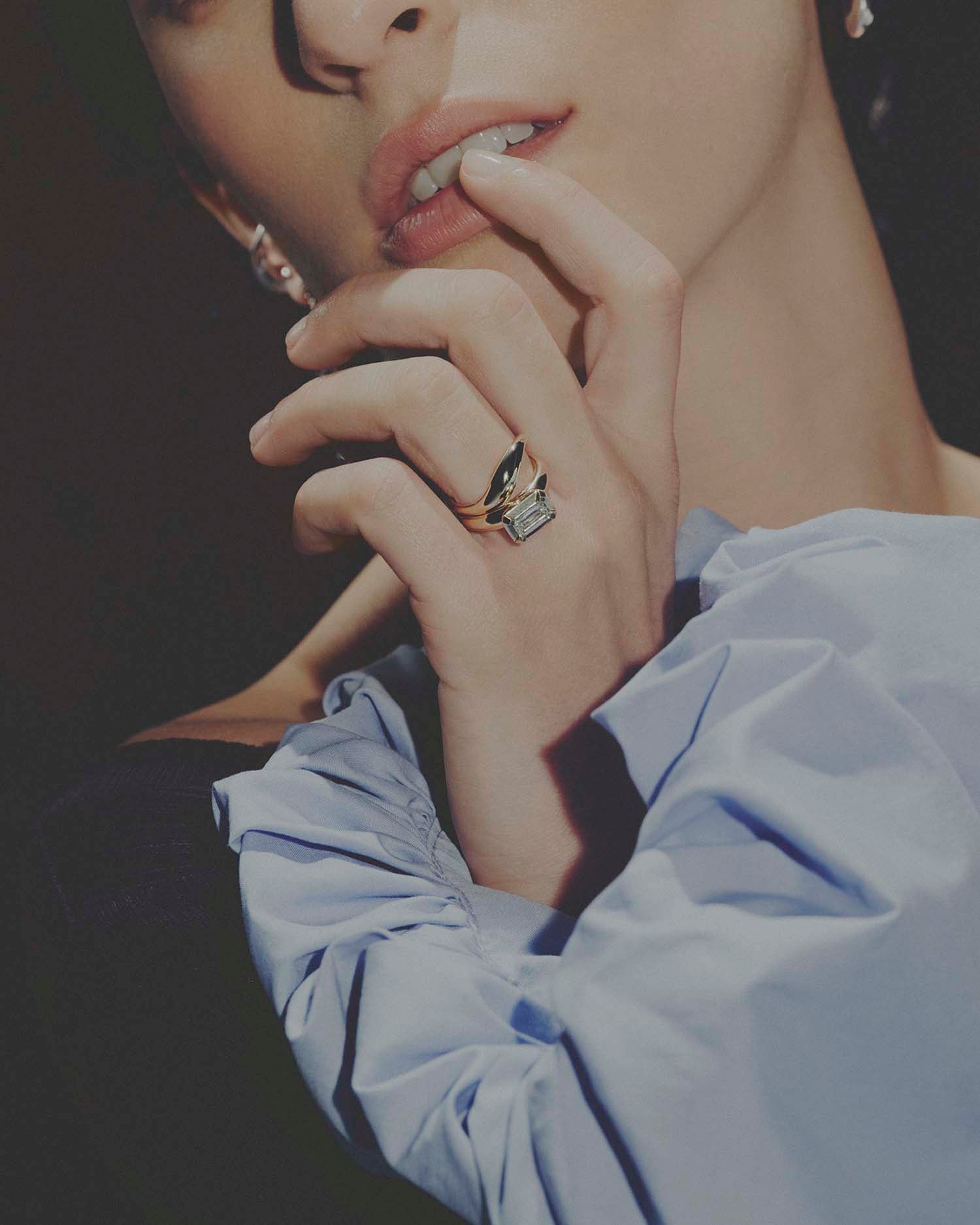 Close-up of a hand wearing a gold ring with a diamond, against a dark background.