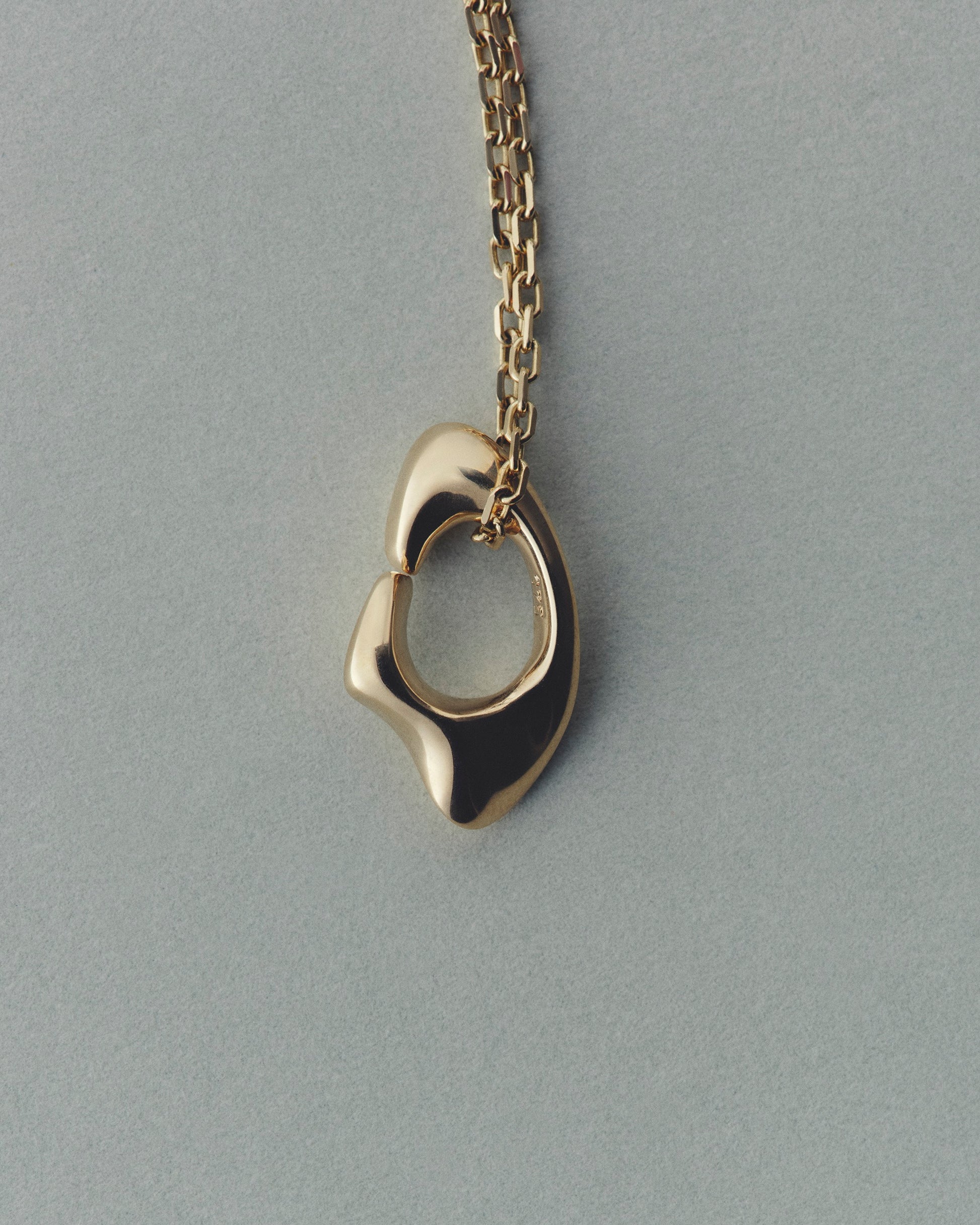 Gold necklace with a unique pendant on a gray background