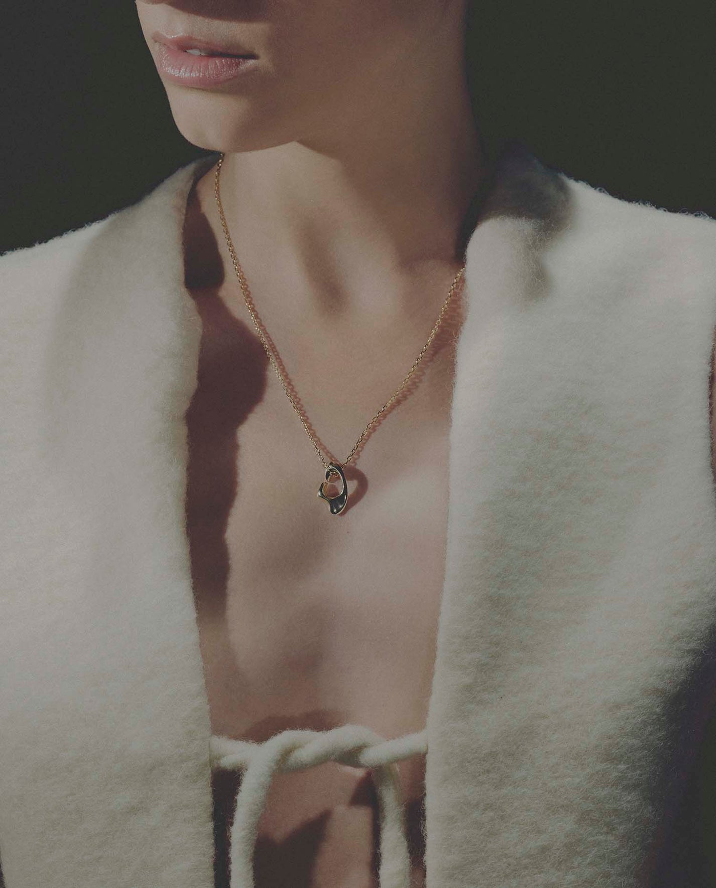 Close-up of a person wearing a necklace with a pendant, set against a dark background.