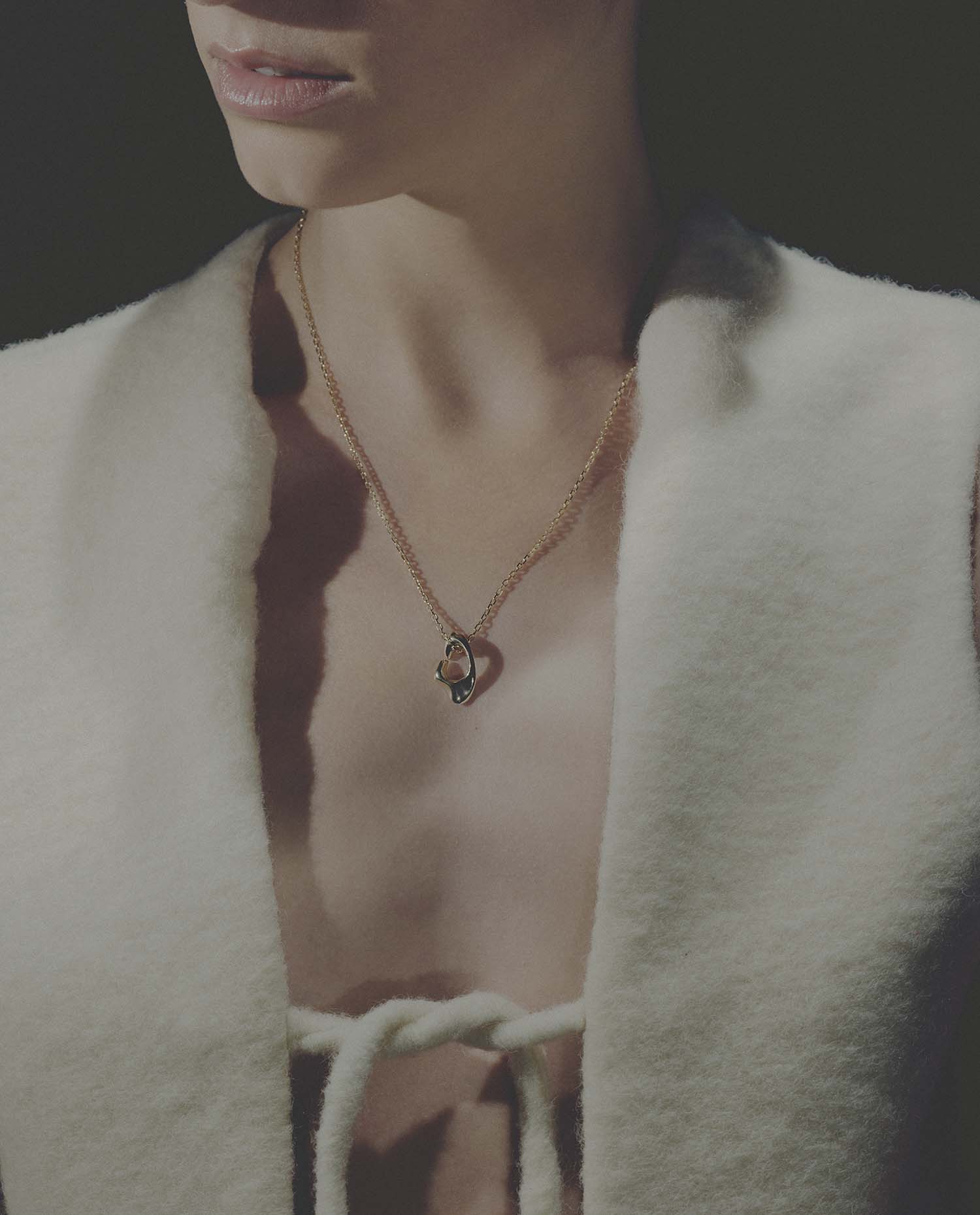 Close-up of a person wearing a necklace with a pendant, set against a dark background.