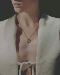 Close-up of a person wearing a necklace with a pendant, set against a dark background.