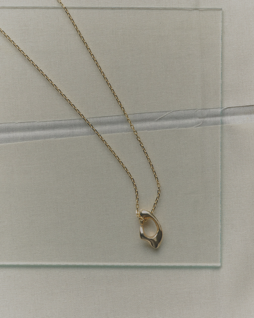 Gold necklace with a unique pendant on a clear glass surface
