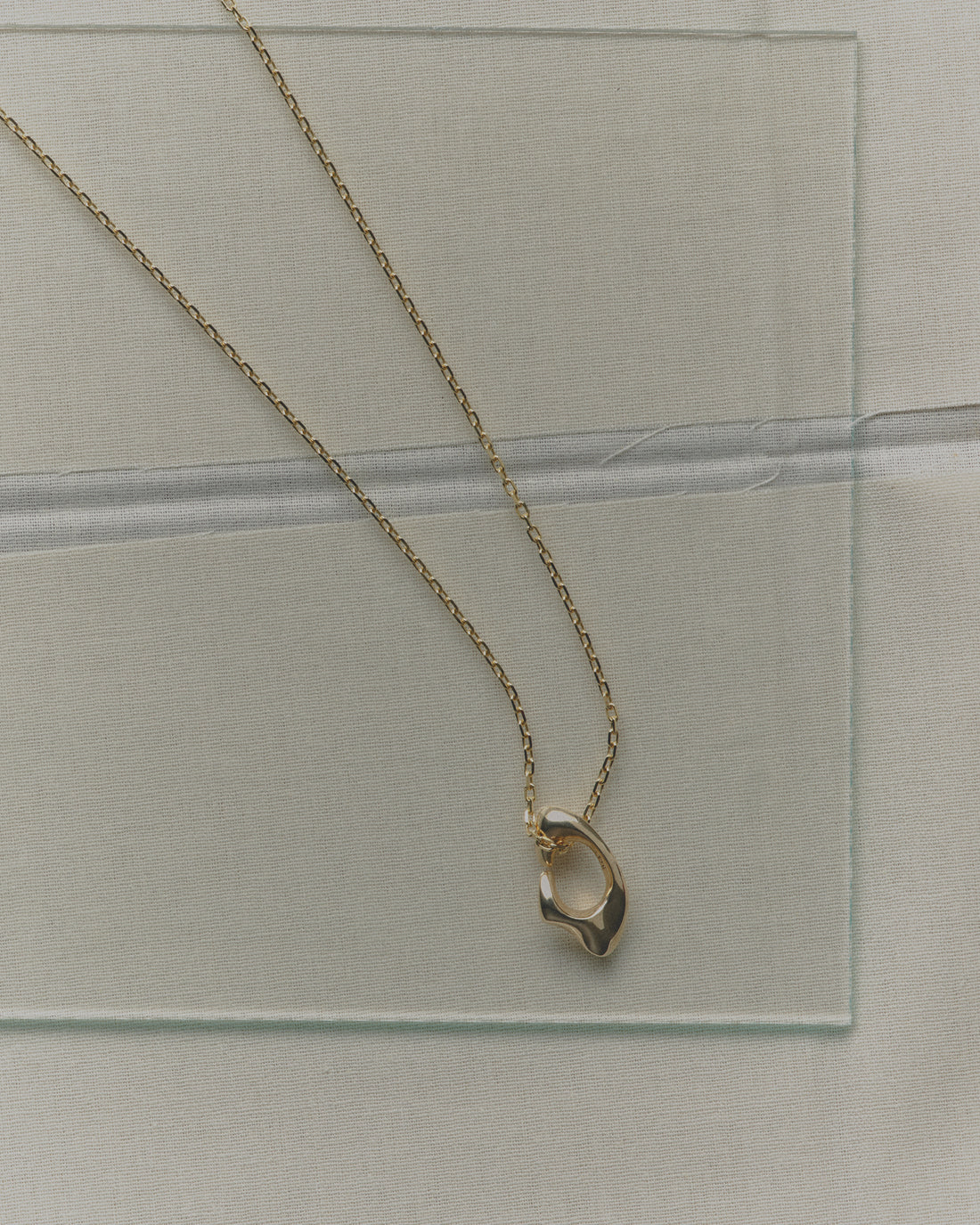 Gold necklace with a unique pendant on a clear glass surface