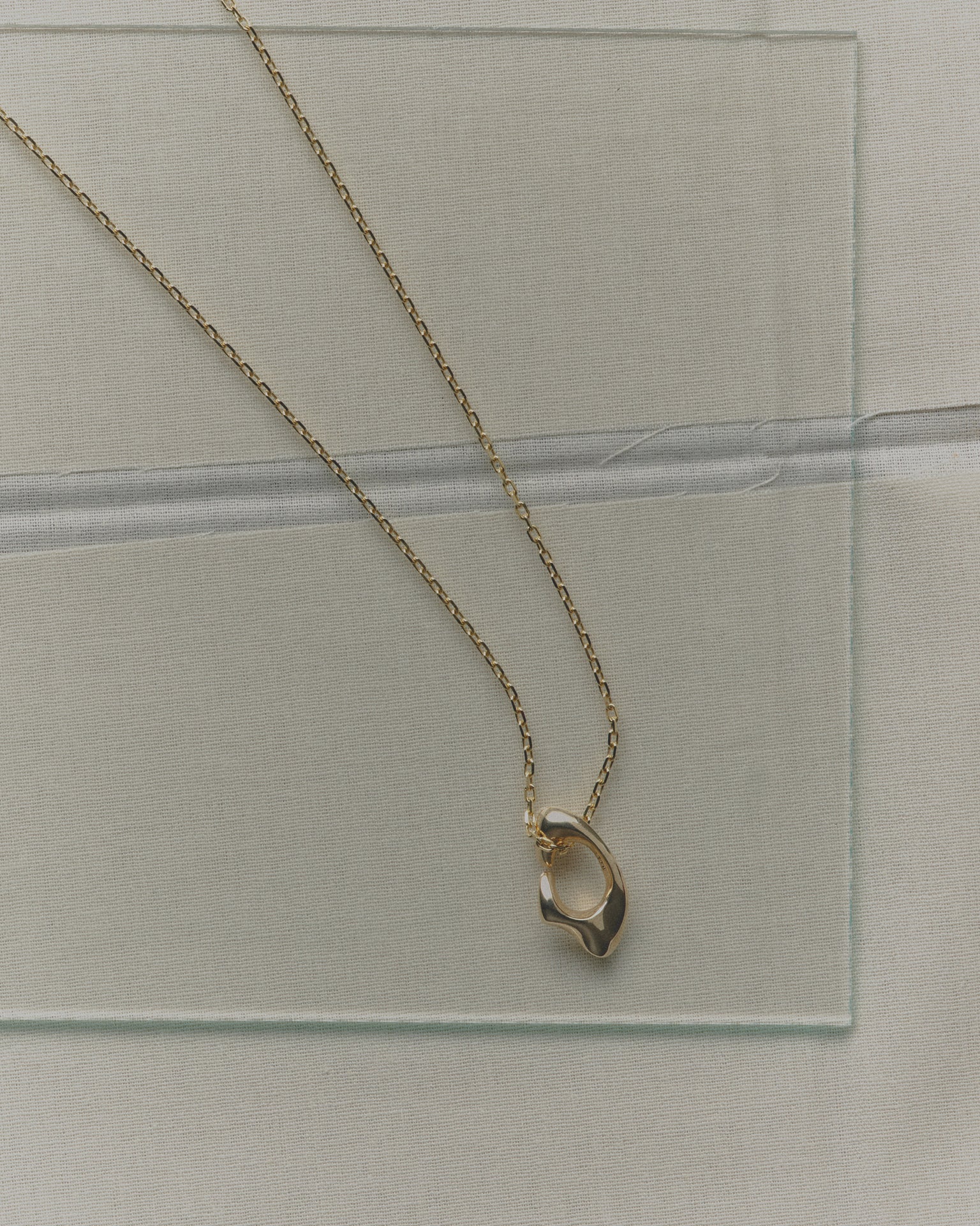 Gold necklace with a unique pendant on a clear glass surface