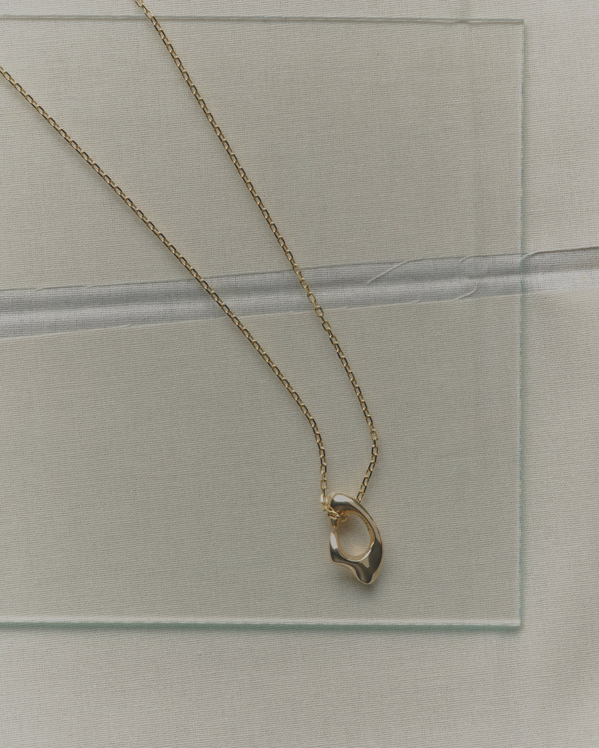 Gold necklace with a unique pendant on a clear glass surface