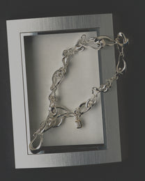 Silver necklace on a reflective surface with a dark background