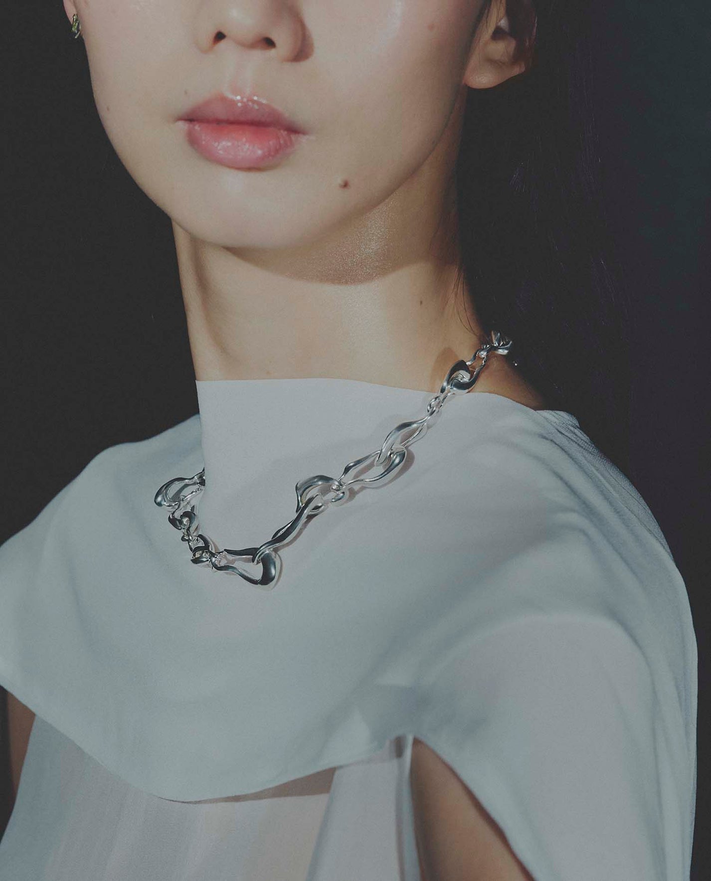 Person wearing a silver chain necklace with a plain background