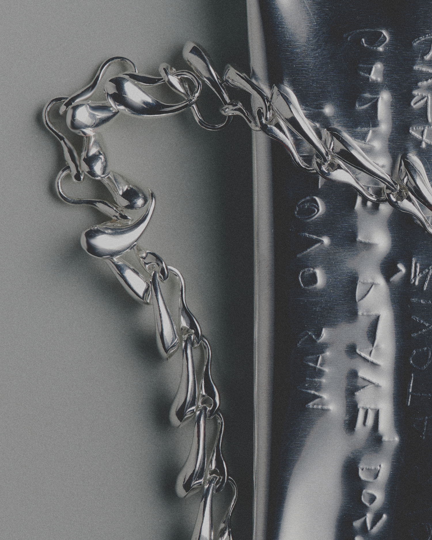 Close-up of a silver necklace with engraved text on a gray background