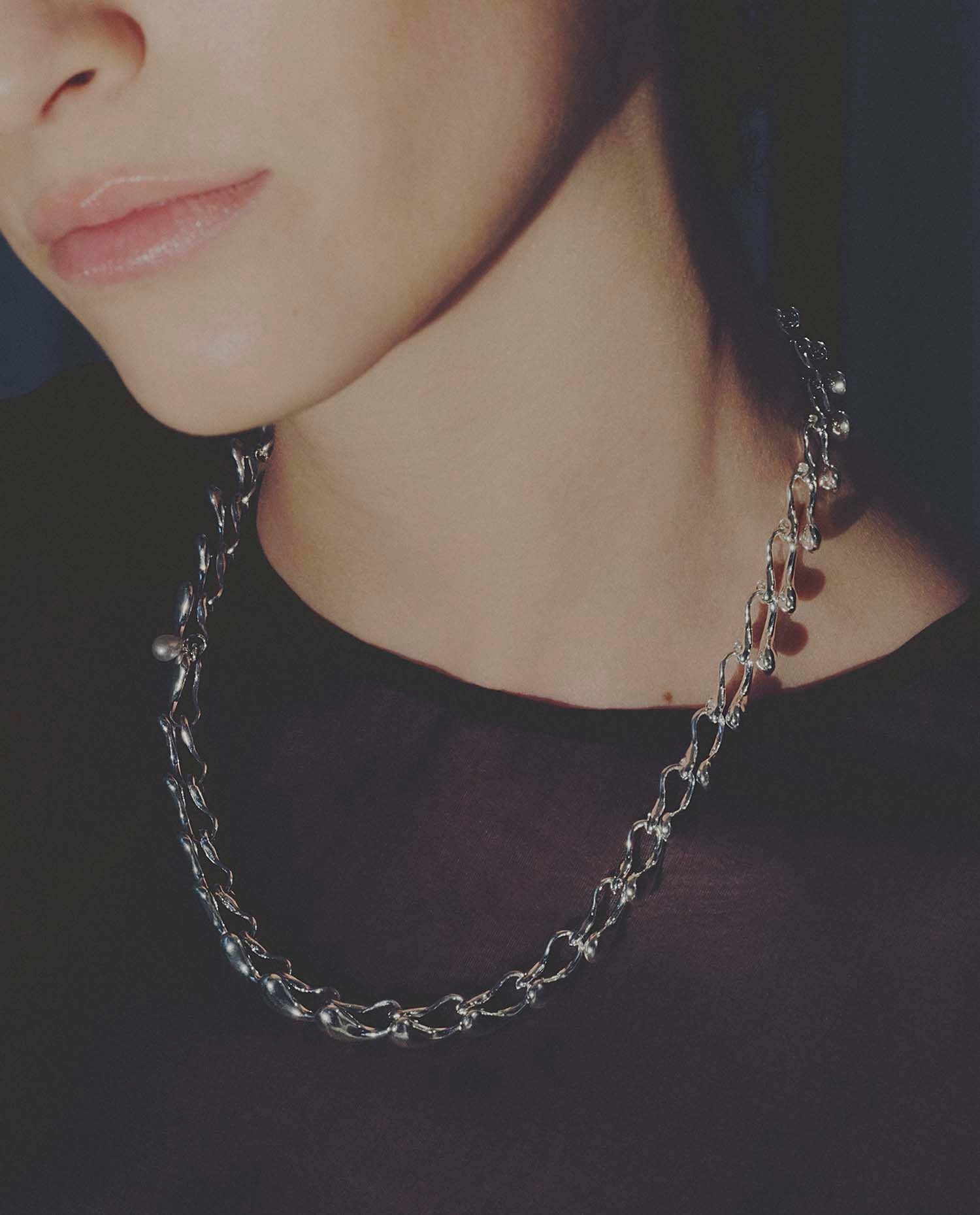 Close-up of a person wearing a silver chain necklace against a dark background
