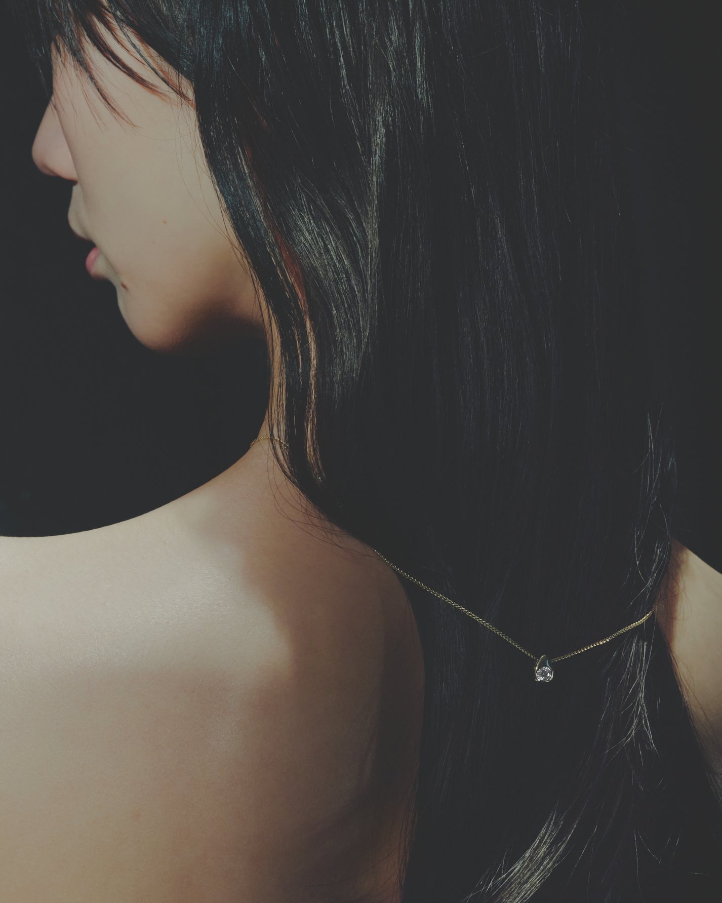 Close-up of a person with a delicate necklace against a dark background