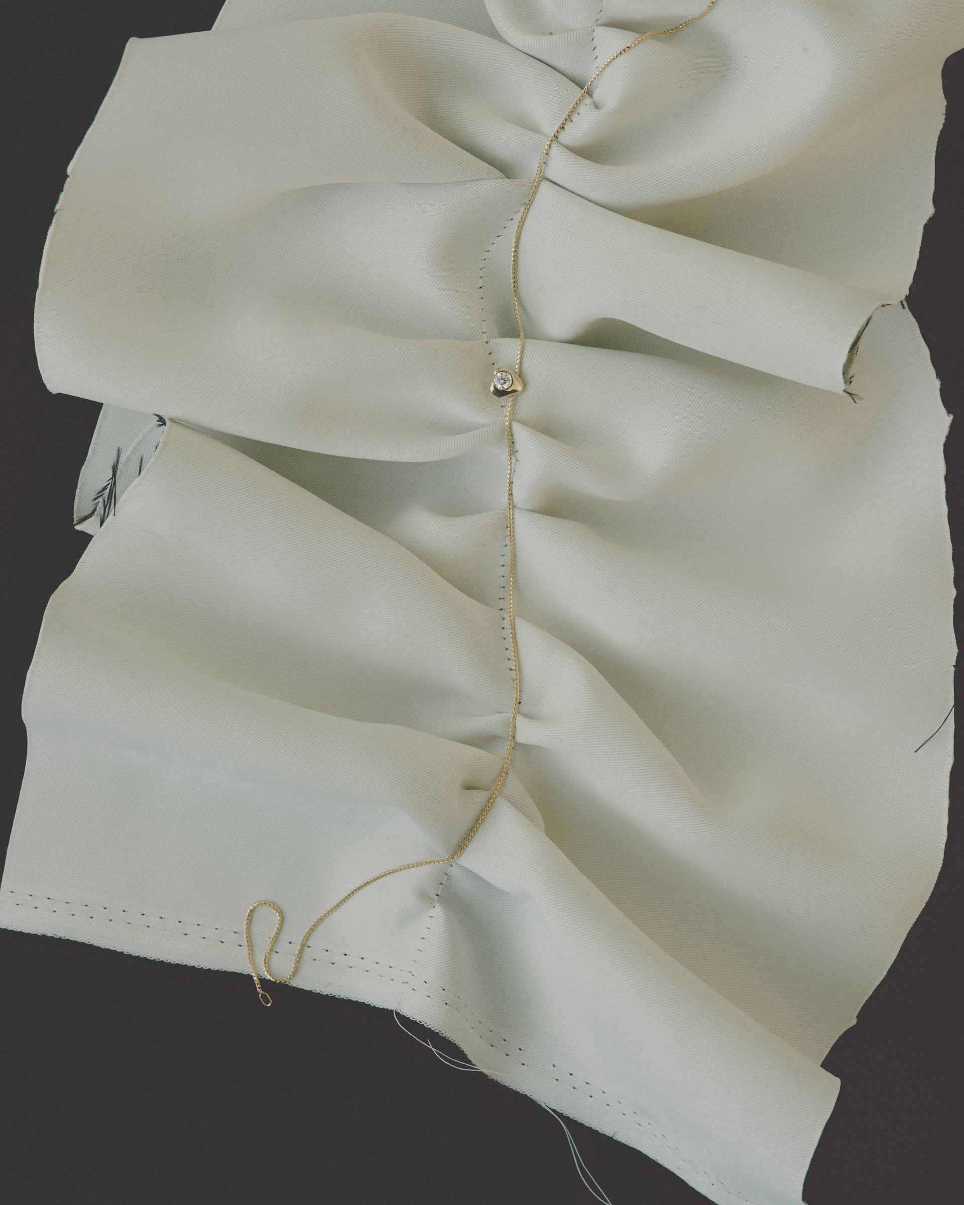 Close-up of a hold diamond necklace on beige fabric with visible stitching on a dark background