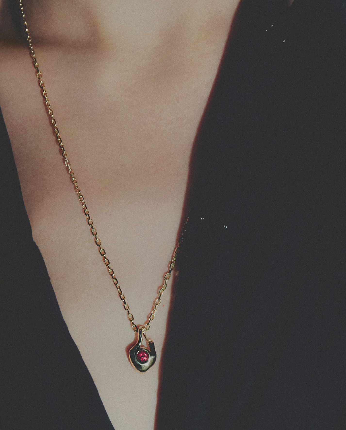 Gold necklace with a red gemstone pendant on a dark background