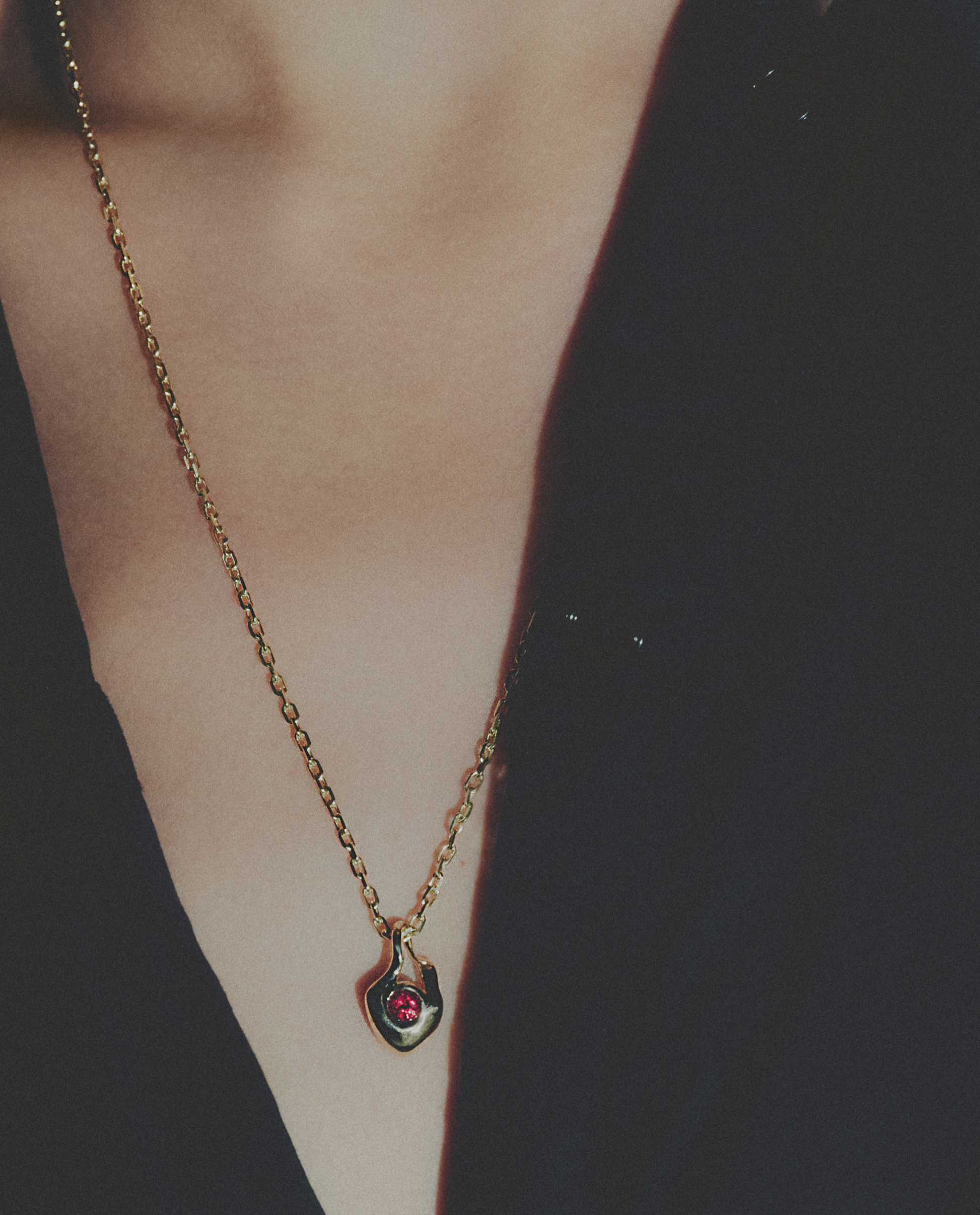 Gold necklace with a red gemstone pendant on a dark background