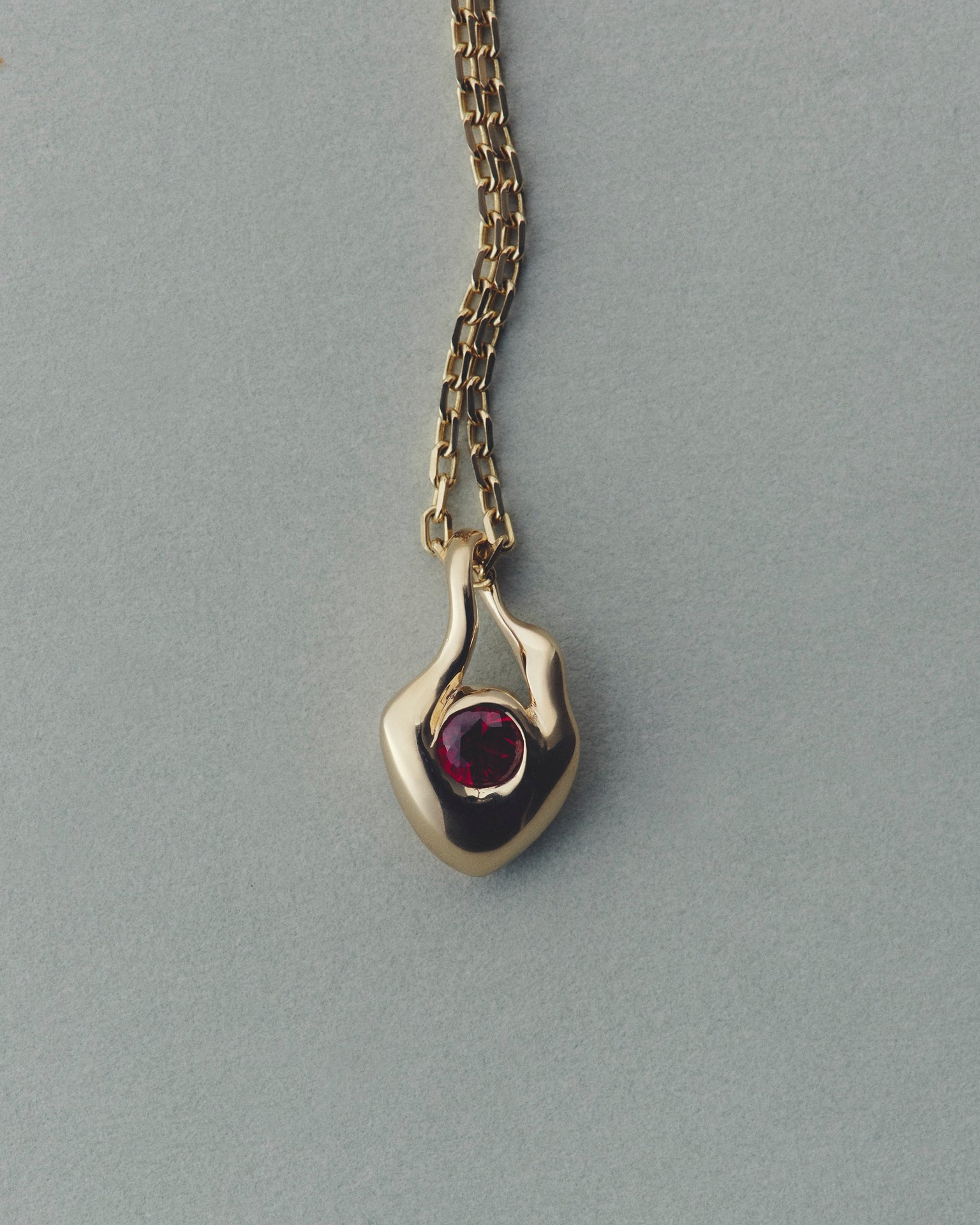 Gold pendant with a red gemstone on a gray background