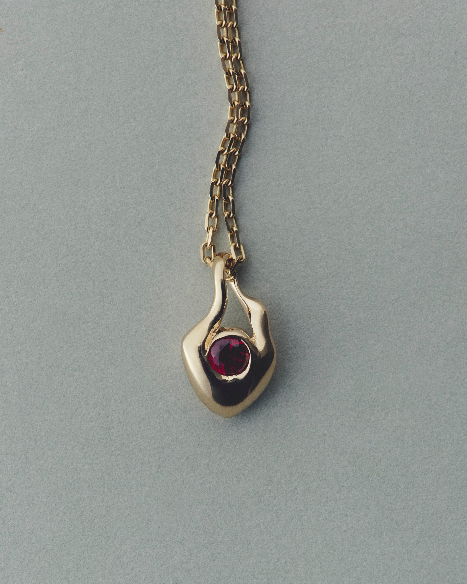 Gold pendant with a red gemstone on a gray background