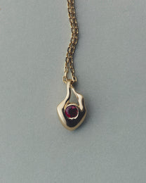 Gold pendant with a red gemstone on a gray background
